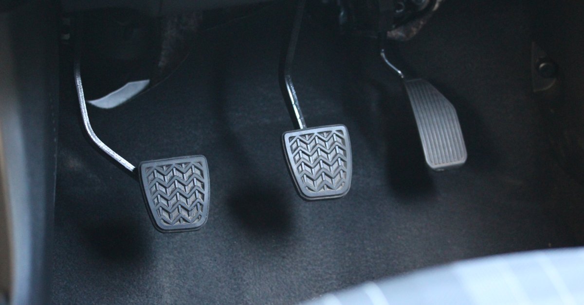 A manual transmission vehicle with a clutch, brake, and accelerator pedals. The car features gray lining behind them.