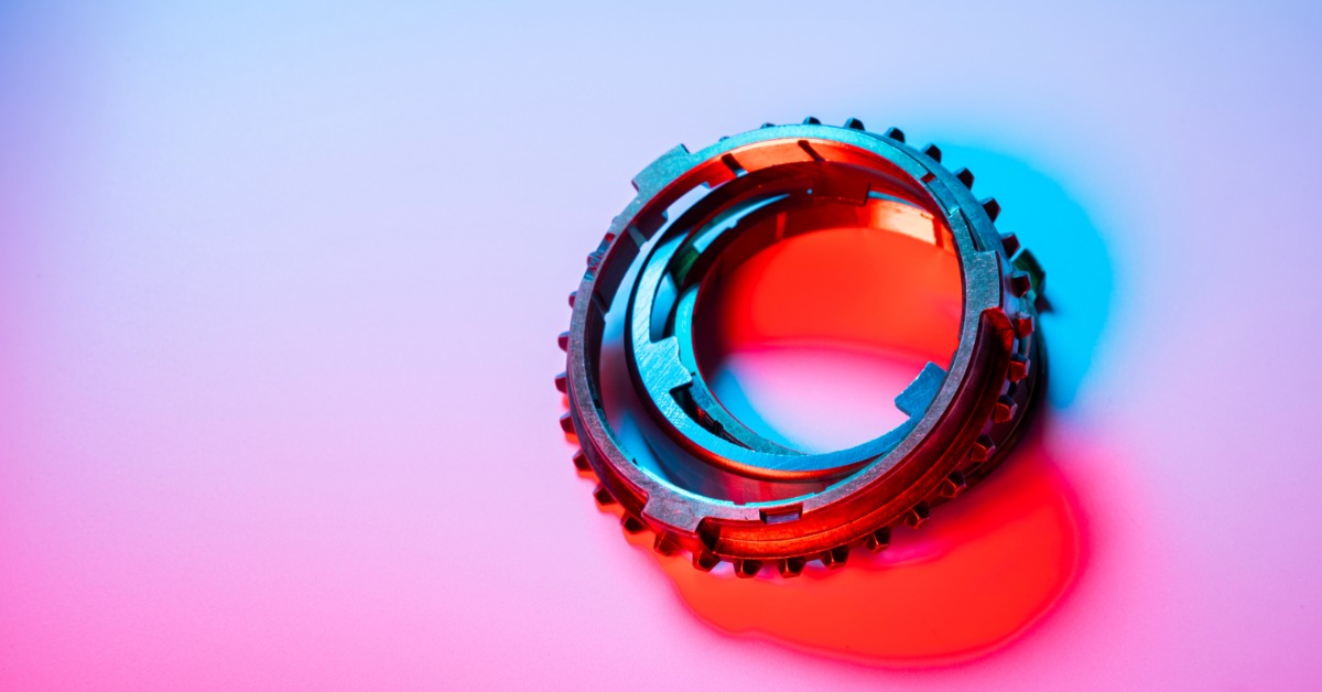 Several metallic transmission synchronizer rings, lit with blue and red light, sit on a pink-and-white surface.