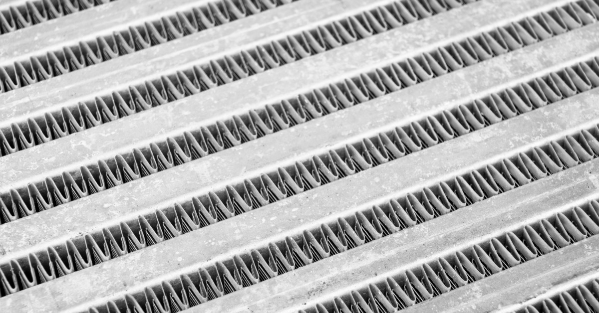 A close-up view of a silver car intercooler surface with repeating metal fins and textured radiator patterns.